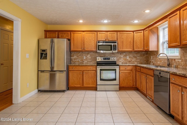 kitchen featuring backsplash, sink, light stone countertops, a textured ceiling, and stainless steel appliances