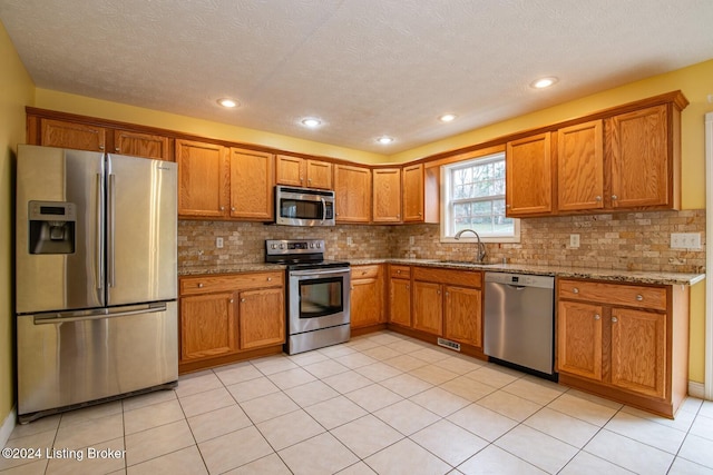 kitchen featuring light stone countertops, sink, a textured ceiling, light tile patterned floors, and appliances with stainless steel finishes