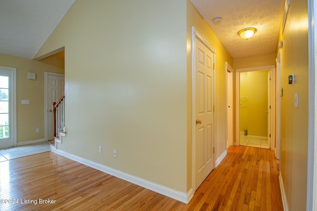 hall featuring lofted ceiling, a textured ceiling, and light hardwood / wood-style flooring