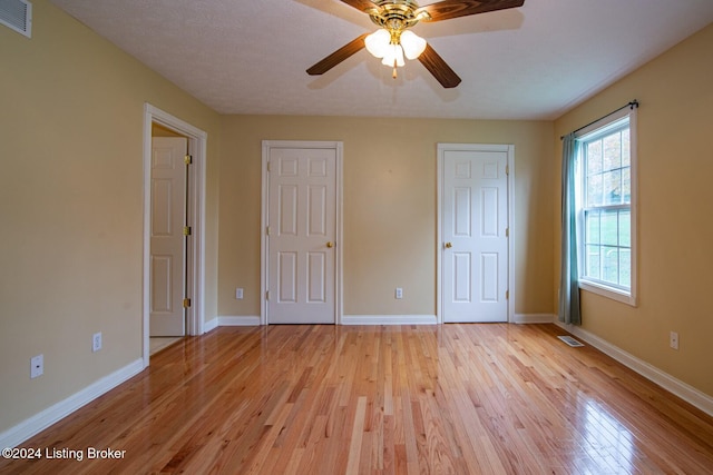 unfurnished bedroom featuring two closets, ceiling fan, light hardwood / wood-style floors, and a textured ceiling