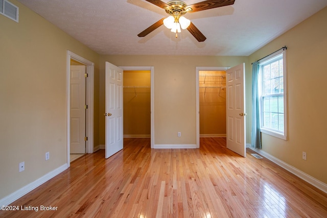 unfurnished bedroom featuring ceiling fan, light hardwood / wood-style floors, a walk in closet, and a textured ceiling