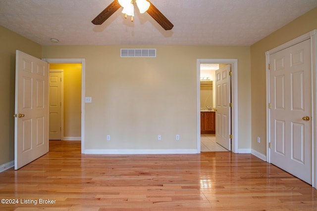 unfurnished bedroom featuring a textured ceiling, light wood-type flooring, ensuite bathroom, and ceiling fan