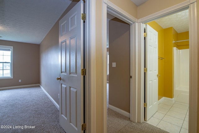 hallway featuring light colored carpet and a textured ceiling