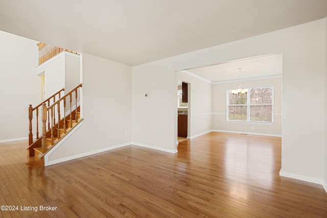 unfurnished living room featuring crown molding, an inviting chandelier, and hardwood / wood-style flooring