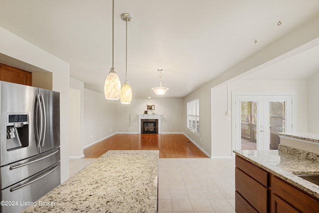 kitchen with french doors, stainless steel refrigerator with ice dispenser, hanging light fixtures, light stone countertops, and light hardwood / wood-style floors