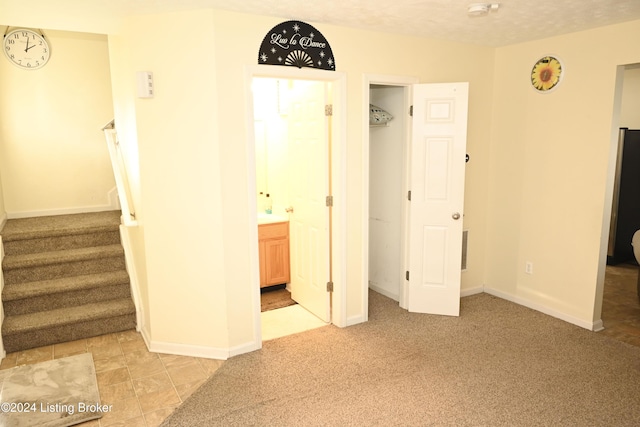 unfurnished bedroom with ensuite bath, light carpet, and a textured ceiling