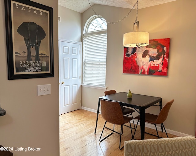 dining space featuring light hardwood / wood-style floors, a textured ceiling, and vaulted ceiling