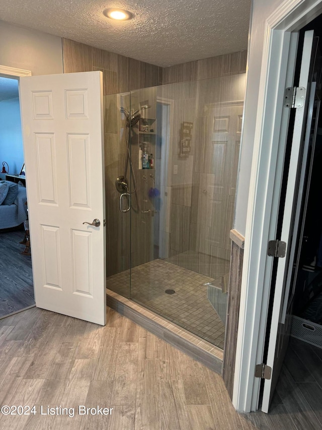 bathroom featuring hardwood / wood-style floors, a shower with shower door, and a textured ceiling