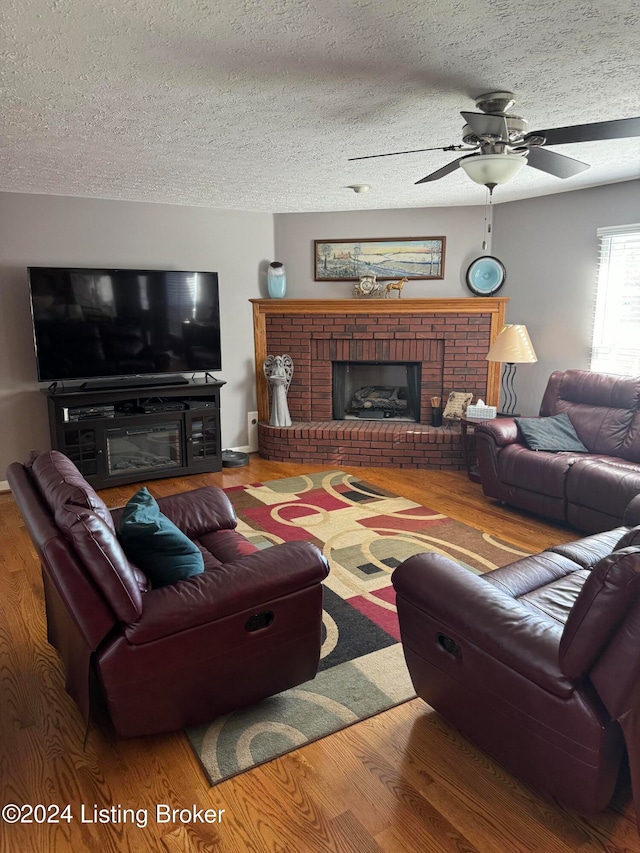 living room featuring a textured ceiling, hardwood / wood-style flooring, a brick fireplace, and ceiling fan