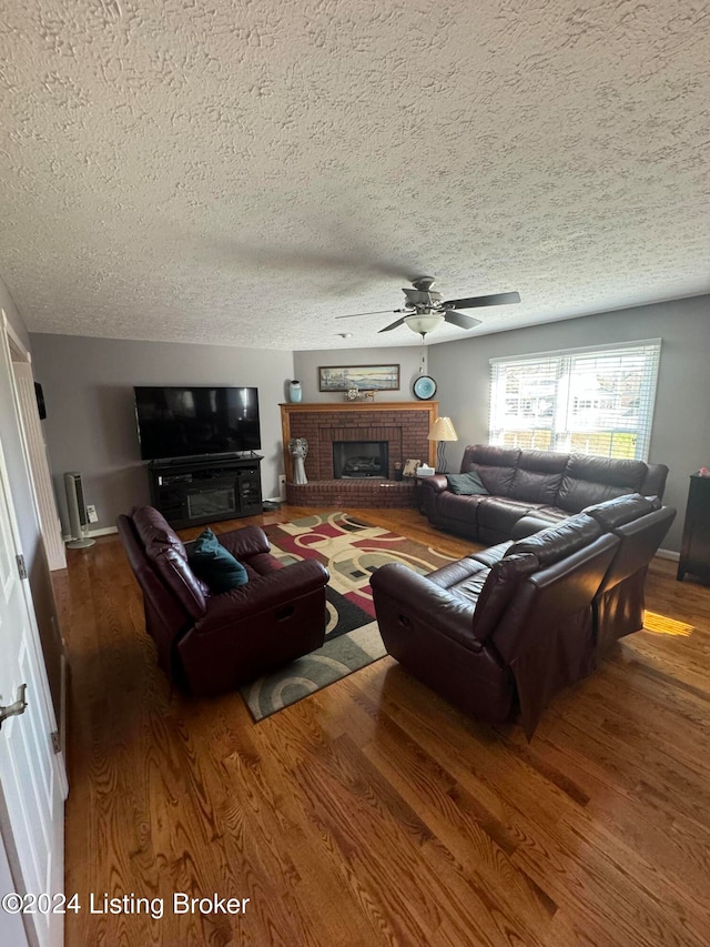 living room featuring a textured ceiling, hardwood / wood-style flooring, a brick fireplace, and ceiling fan