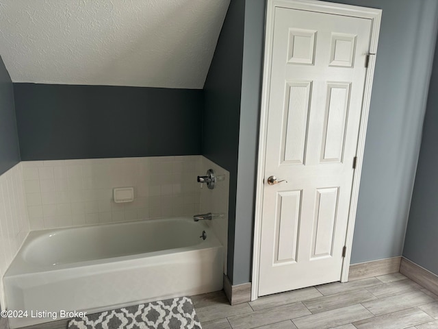 bathroom featuring a washtub, a textured ceiling, and vaulted ceiling