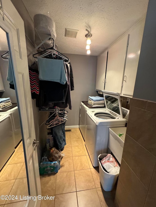 clothes washing area with cabinets, a textured ceiling, sink, light tile patterned floors, and separate washer and dryer