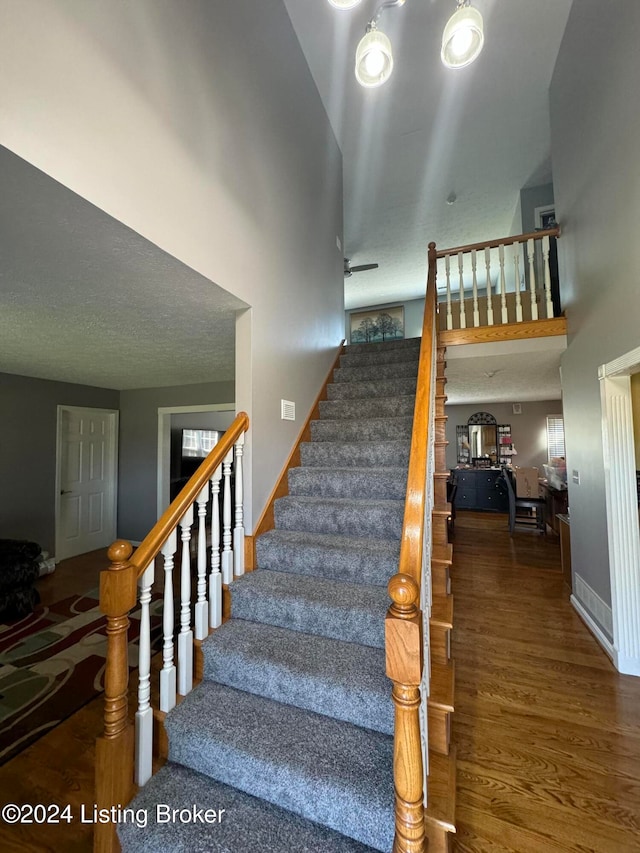 stairway with wood-type flooring and a high ceiling