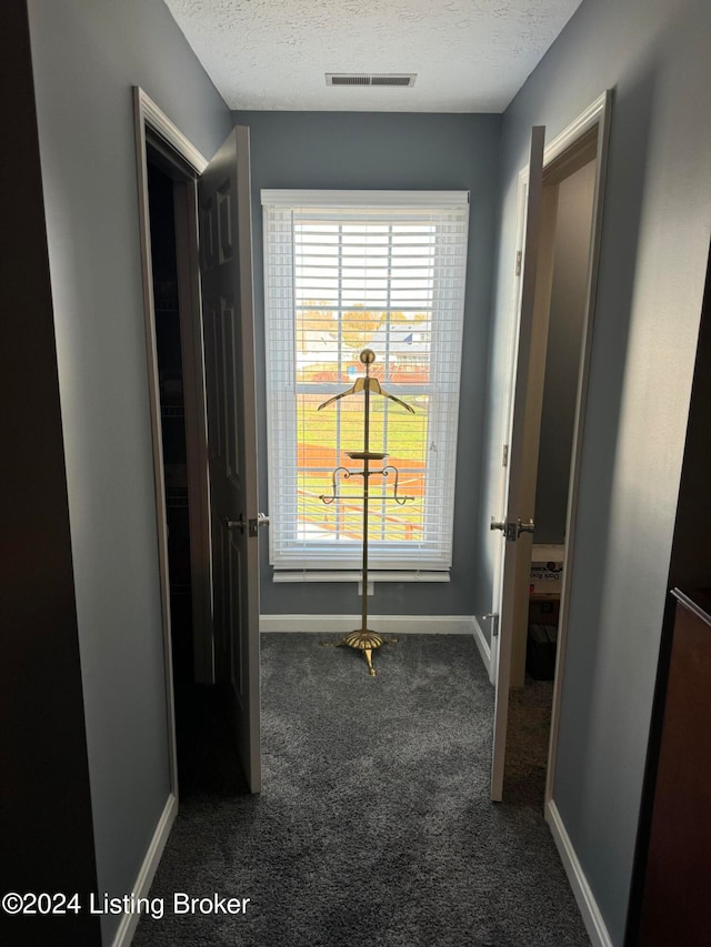 corridor featuring a textured ceiling and dark carpet