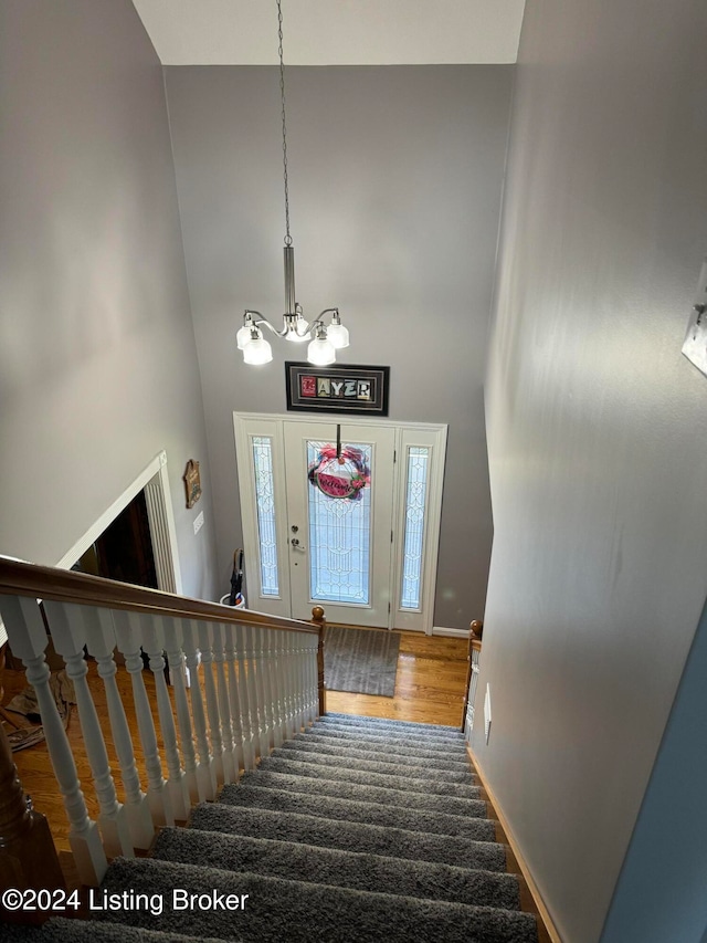 stairs featuring hardwood / wood-style floors, a towering ceiling, and a chandelier