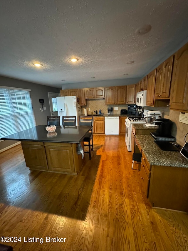 kitchen with hardwood / wood-style floors, a center island, white appliances, decorative backsplash, and a textured ceiling