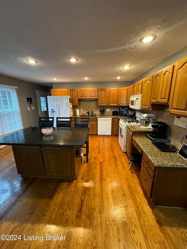 kitchen featuring a textured ceiling, hardwood / wood-style floors, a center island, and white appliances