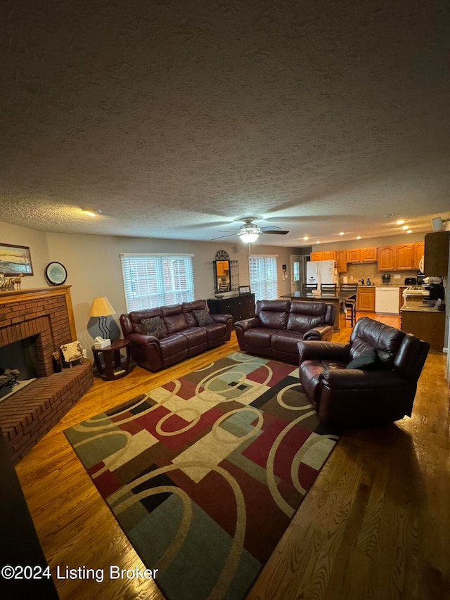 living room featuring plenty of natural light, wood-type flooring, a textured ceiling, and a brick fireplace