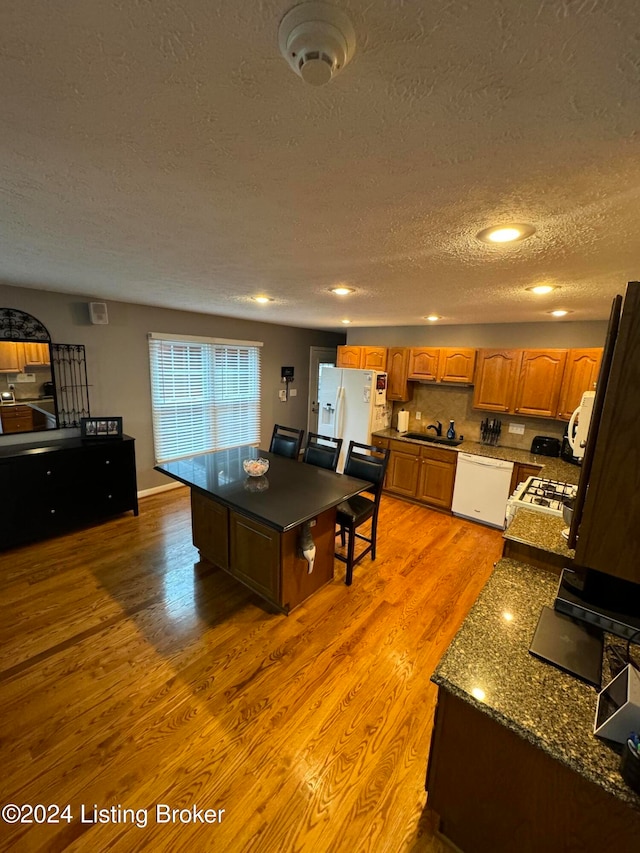 kitchen with white appliances, a textured ceiling, sink, wood-type flooring, and a center island