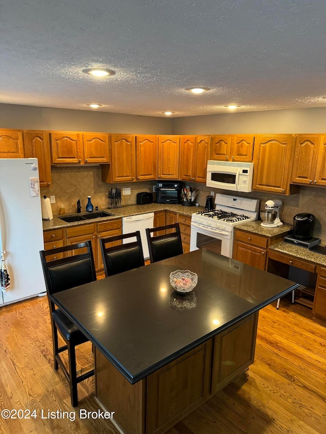 kitchen featuring a center island, light hardwood / wood-style floors, a textured ceiling, white appliances, and decorative backsplash