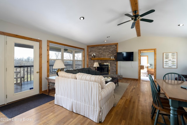 living room with a stone fireplace, ceiling fan, lofted ceiling with beams, and hardwood / wood-style flooring