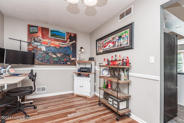 home office with light hardwood / wood-style floors and a textured ceiling