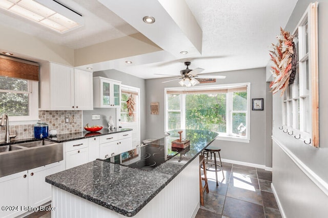 kitchen with decorative backsplash, black electric cooktop, white cabinetry, and dark stone counters