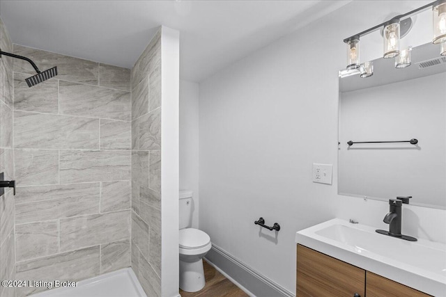 bathroom with hardwood / wood-style floors, vanity, toilet, and tiled shower