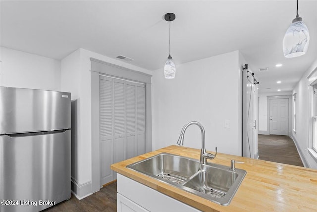 kitchen featuring dark wood-type flooring, wooden counters, sink, stainless steel fridge, and a barn door