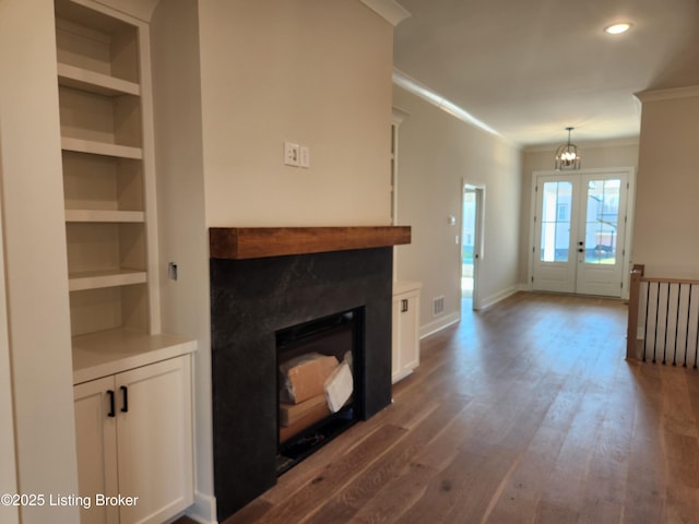 unfurnished living room featuring built in shelves, dark wood-type flooring, a fireplace, baseboards, and crown molding