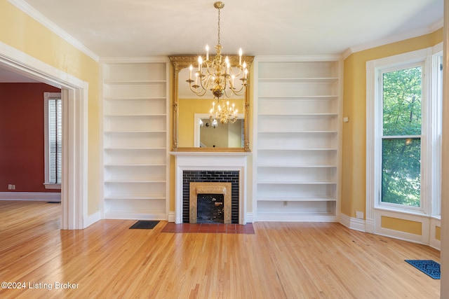 unfurnished living room featuring built in shelves, crown molding, hardwood / wood-style floors, and an inviting chandelier