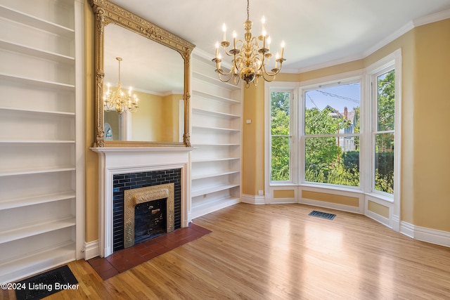 unfurnished living room with a tile fireplace, built in shelves, an inviting chandelier, crown molding, and hardwood / wood-style flooring