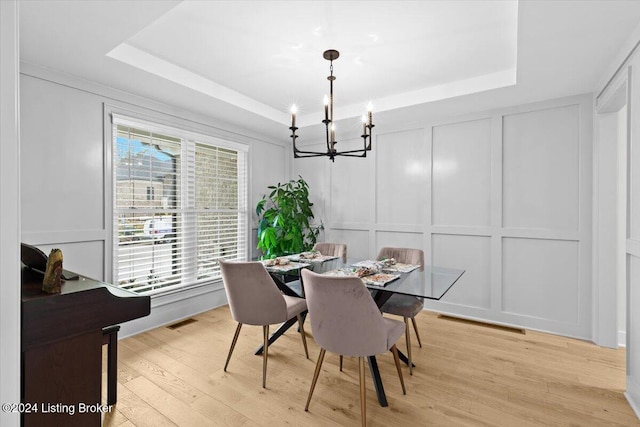 dining area with a tray ceiling, a chandelier, and light wood-type flooring