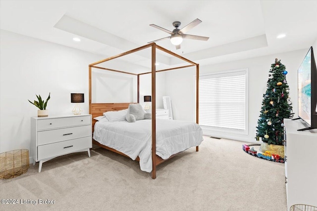 bedroom with a raised ceiling, ceiling fan, and light colored carpet