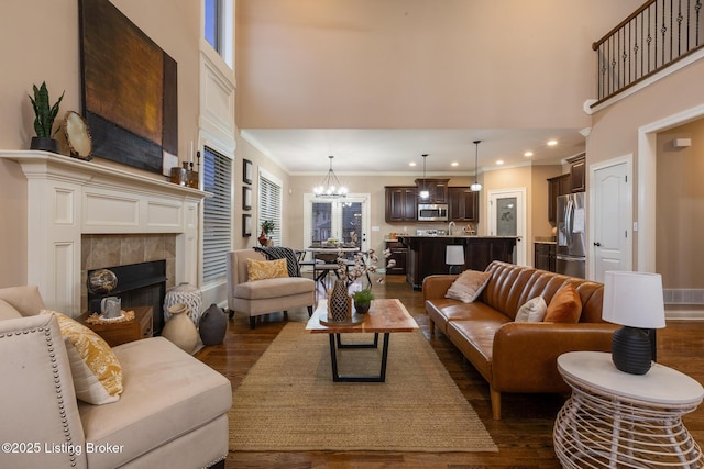 living area featuring dark wood-type flooring, ornamental molding, a towering ceiling, and an inviting chandelier