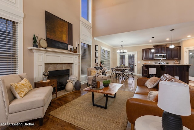 living room featuring dark wood-style flooring, a notable chandelier, crown molding, a tile fireplace, and baseboards