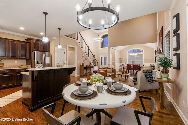 dining space featuring dark wood-style flooring, crown molding, a towering ceiling, an inviting chandelier, and stairs