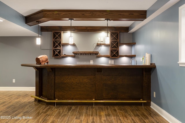 bar with dark wood-style floors, hanging light fixtures, bar area, and baseboards