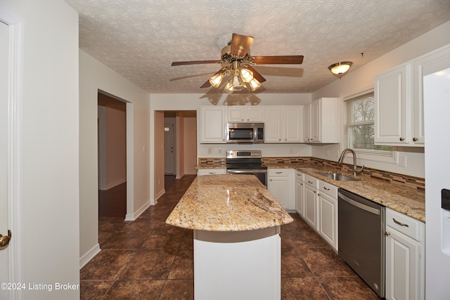 kitchen featuring sink, white cabinetry, a kitchen island, stainless steel appliances, and light stone countertops