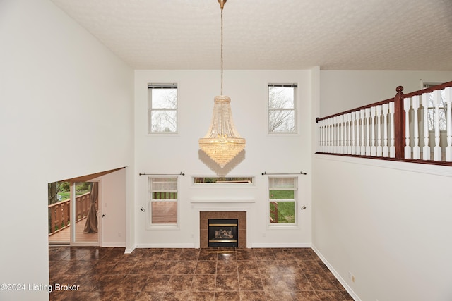 unfurnished living room with a towering ceiling, a fireplace, a chandelier, and a textured ceiling