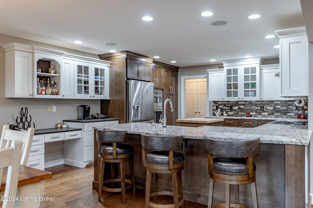 kitchen featuring a kitchen bar, light stone countertops, stainless steel appliances, light hardwood / wood-style floors, and white cabinetry