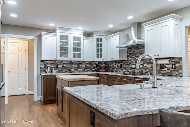 kitchen featuring wood counters, tasteful backsplash, wall chimney range hood, a center island, and white cabinetry