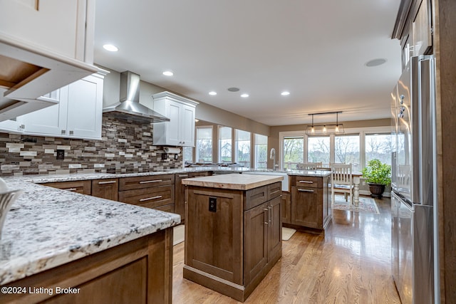 kitchen featuring stainless steel fridge, white cabinetry, a kitchen island, and wall chimney exhaust hood