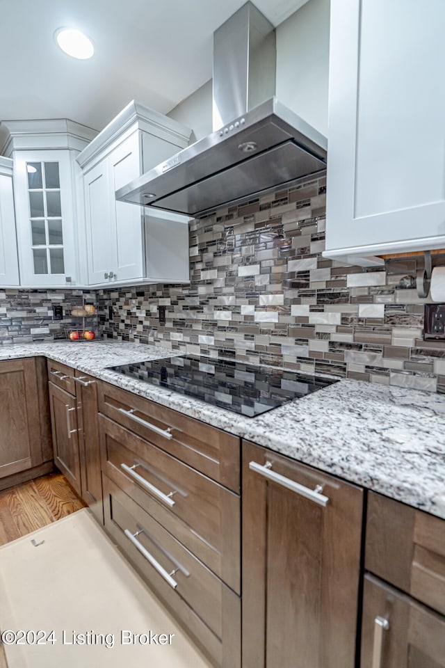 kitchen featuring decorative backsplash, light wood-type flooring, wall chimney exhaust hood, black electric cooktop, and white cabinetry