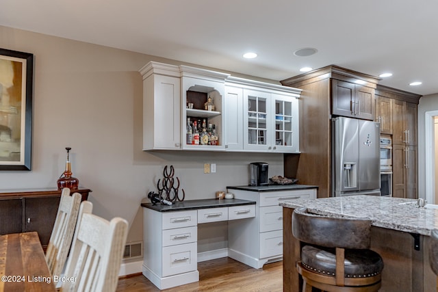 kitchen with dark stone counters, white cabinetry, stainless steel appliances, and light hardwood / wood-style floors