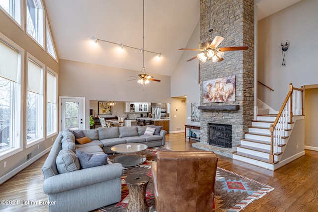 living room with high vaulted ceiling, track lighting, ceiling fan, a fireplace, and wood-type flooring