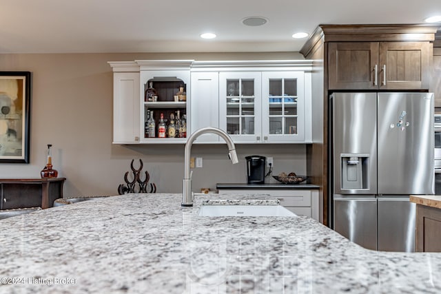 kitchen featuring light stone countertops, sink, white cabinetry, and stainless steel refrigerator with ice dispenser