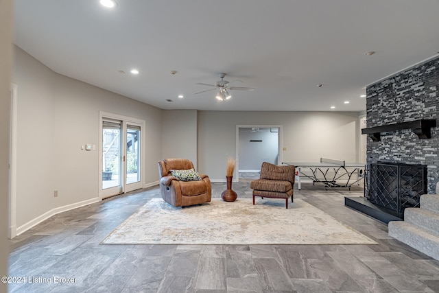 living area featuring a stone fireplace and ceiling fan