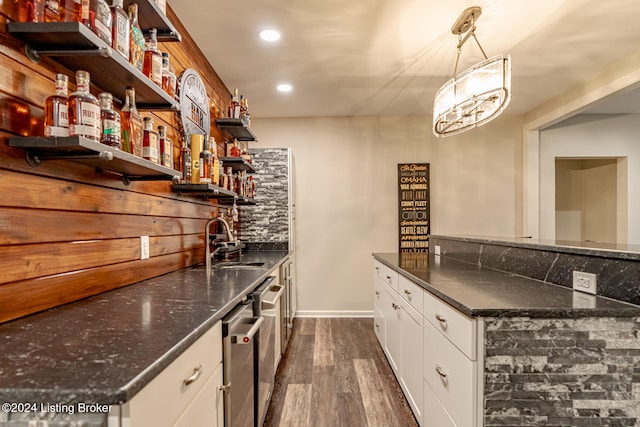 bar featuring dark stone counters, sink, dark hardwood / wood-style floors, white cabinetry, and hanging light fixtures