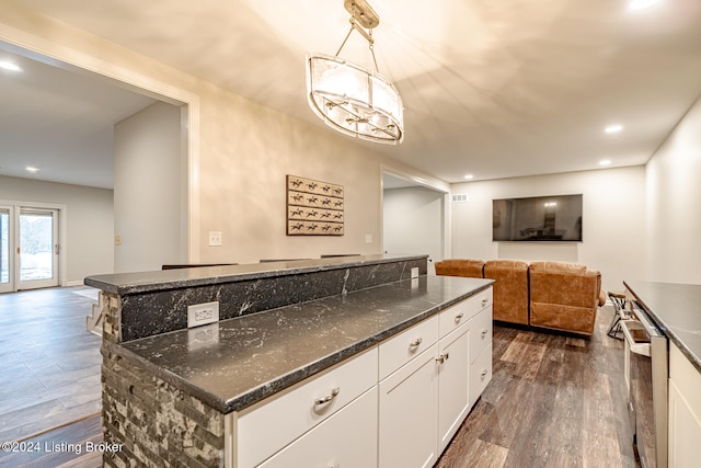 kitchen with pendant lighting, dark stone countertops, white cabinets, dark hardwood / wood-style floors, and a kitchen island